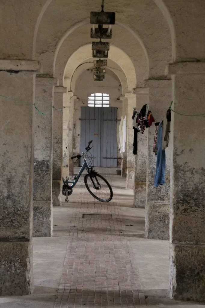 Ein Fahrrad steht in einem alten, gewölbten Gang mit Steinpfeilern. An einer Leine hängen Kleidungsstücke.