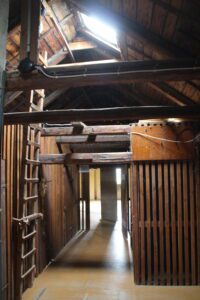 Dunkler Dachbodenflur mit Holzlatten, sichtbaren Balken und einer Leiter unter einem kleinen Dachfenster.