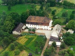 Luftaufnahme einer ländlichen Hofanlage mit großen Gebäuden, Gärten und umgebenden Grünflächen.