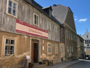 Altes Schwesternhaus mit Holzfassade und großem Jubiläumsbanner an einer leicht ansteigenden Gasse.