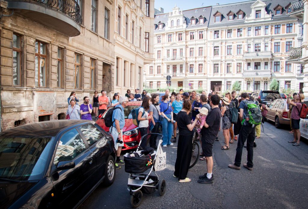 Eine größere Gruppe von Menschen steht in einer Altstadtstraße zwischen Wohnhäusern und schaut sich um.