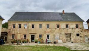 Altes, unverputztes Wohnhaus mit Solarpanels auf dem Dach und Hofbereich.