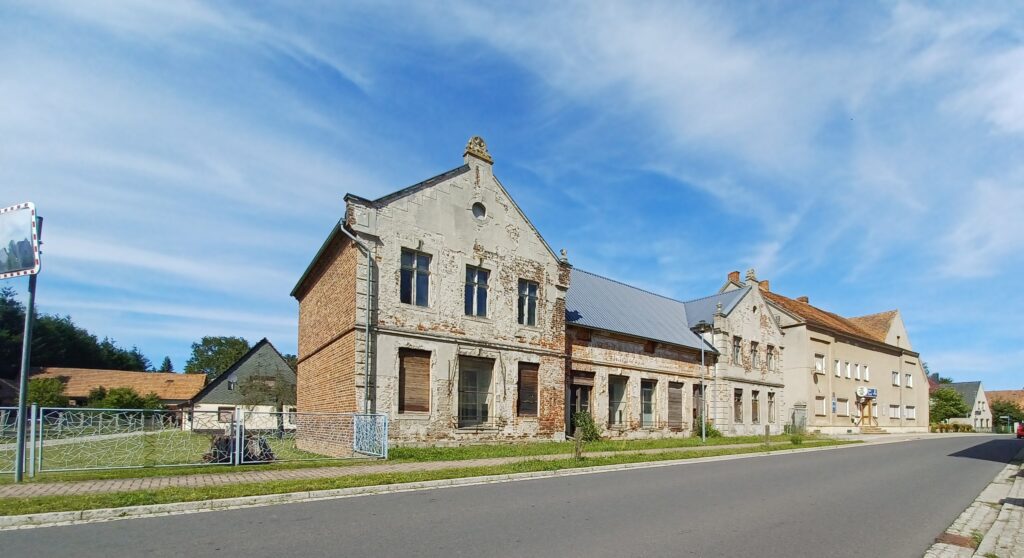 Straßenansicht mit einem alten, verfallenen Gebäude im Vordergrund mit zum Teil verschlossenen Fenstern.