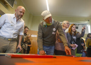 Mehrere Erwachsene stehen in einem Raum um einen Tisch und diskutieren gemeinsam über bunte Karten und Materialien.