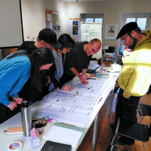 Fünf Personen stehen um einen Tisch und arbeiten gemeinsam an einem großen Planungsblatt mit Notizen.