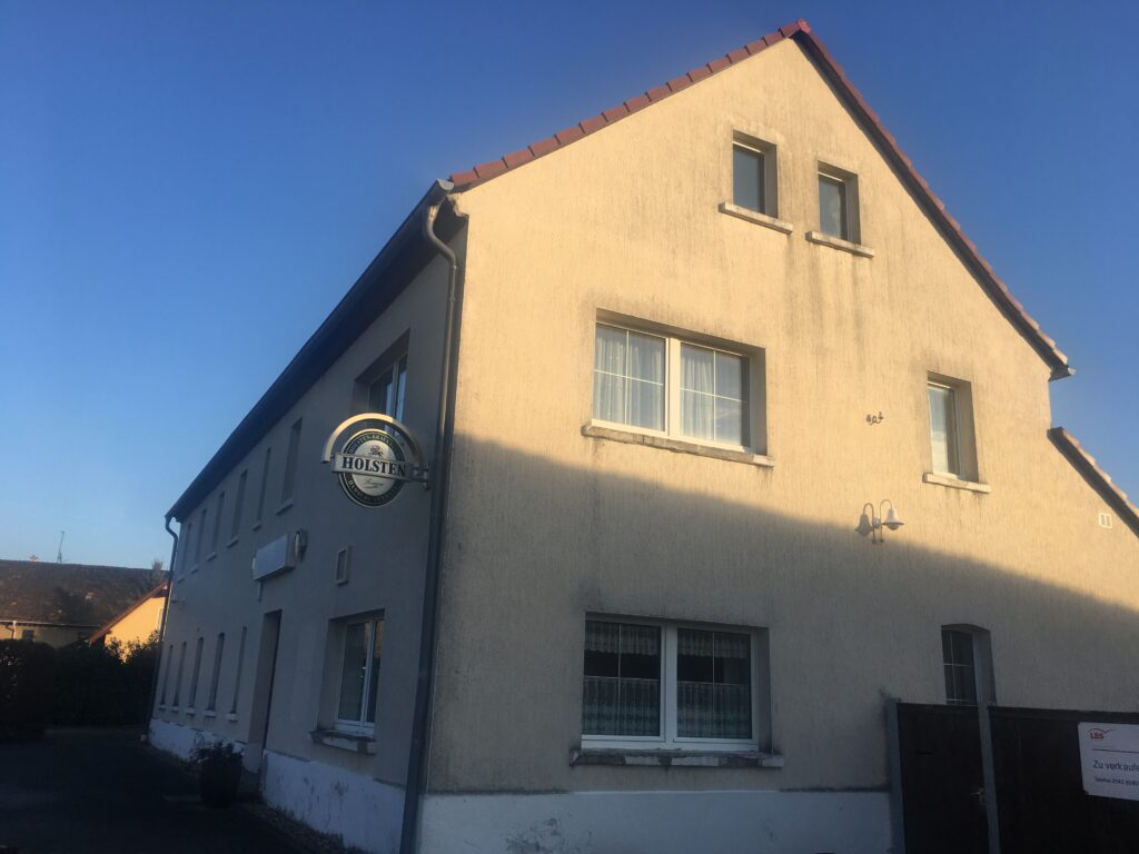 Altes Gasthaus mit heller Fassade und Holsten-Schild an der Wand.