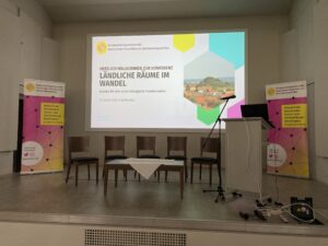 Bühne mit vier Stühlen, Rednerpult und Leinwand bei Konferenz ‘Ländliche Räume im Wandel’ in Weißenfels.
