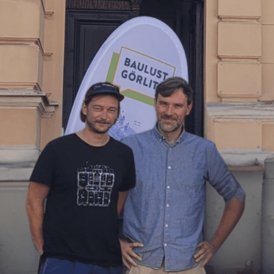 Foto von Raffael Hermann und Daniel Sauer die nebeneinander stehen vor einer Fahne mit der Aufschrift Baulust Görlitz.