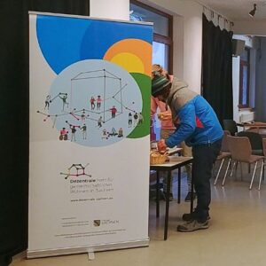 Zwei Personen stehen an einem Tisch neben einem Rollbanner der Dezentrale - Netzwerk für gemeinschaftlichen Wohnens in Sachsen.