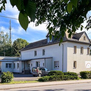 Außenansicht auf ein Haus mit heller Fassade, davor steht ein Auto.